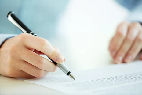 Hand hält einen Stift und hält diesen über einen Vertrag.